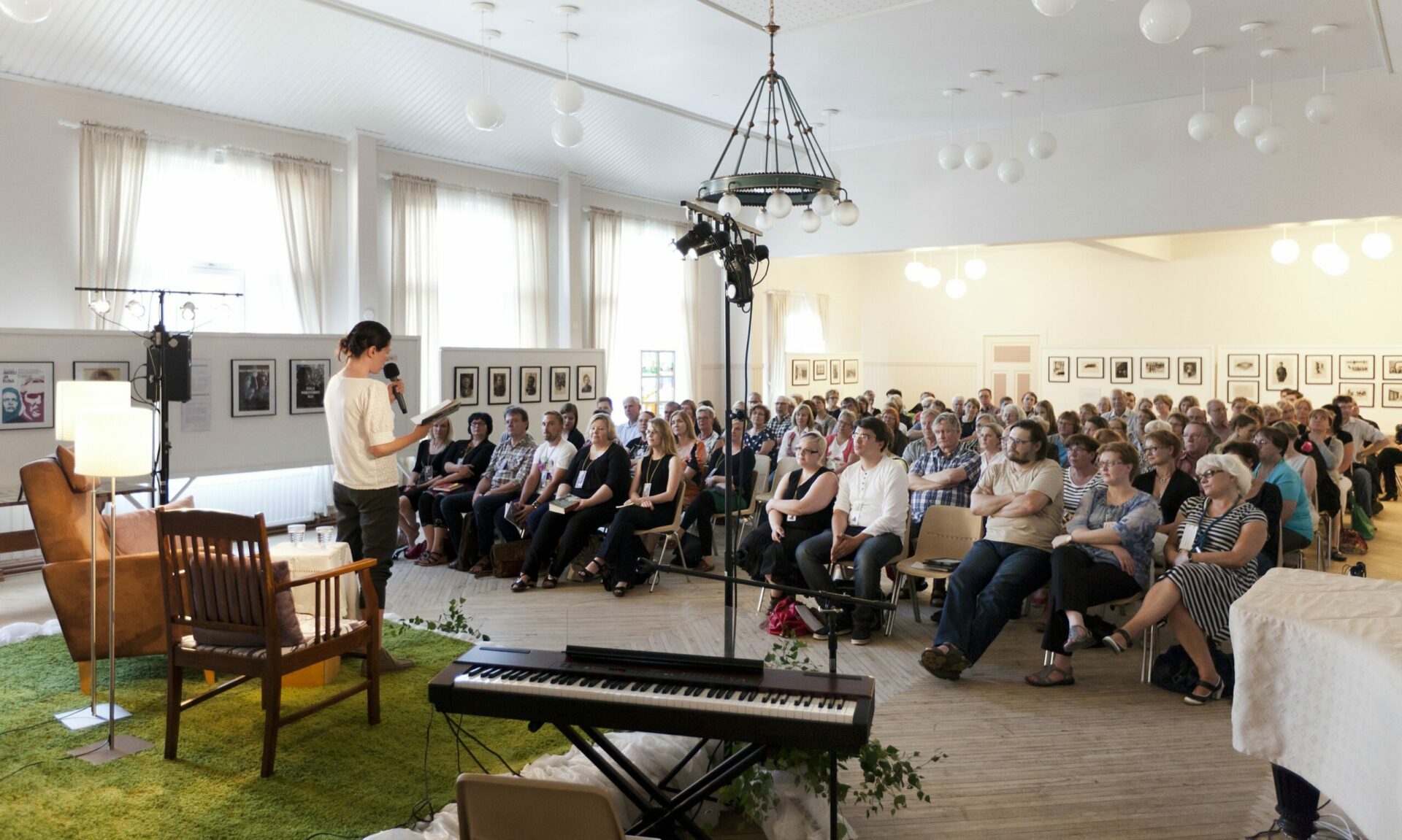 Kirjailija esiintymässä Pentinkulman päivillä. Kuva on otettu kirjailijan takaa lavalta, yleisö istuu tuoleilla kasvot kameraan.