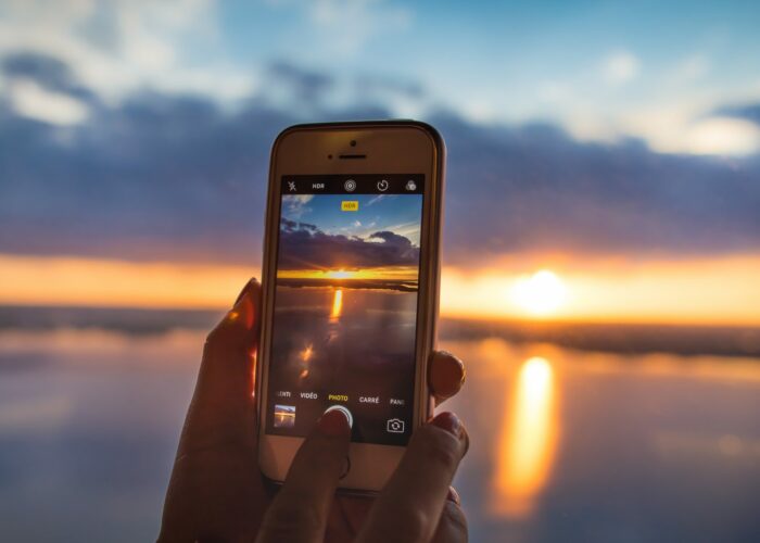 Valokuva puhelimesta, jolla otetaan kuvaa auringonlaskusta Näsijärvellä. Kuva on otettu Näsinneulan näkötornissa.