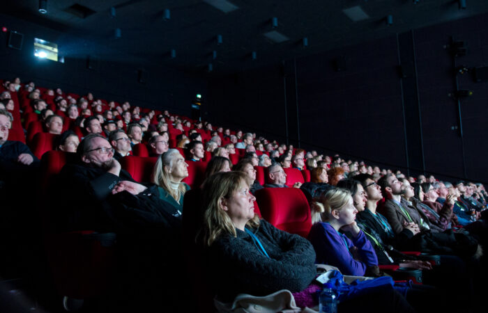 Elokuvasali täynnä yleisöä hämärässä valaistuksessa