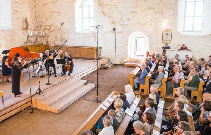 Ihmisiä kuuntelemassa konserttia vanhassa kivikirkossa