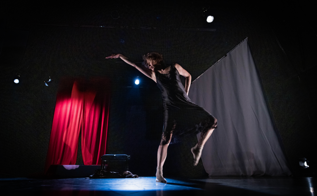 Anniina Kumpuniemi tanssii tummalla näyttämöllä, taustalla valo osuu punaiseen ja mustaan verhoon