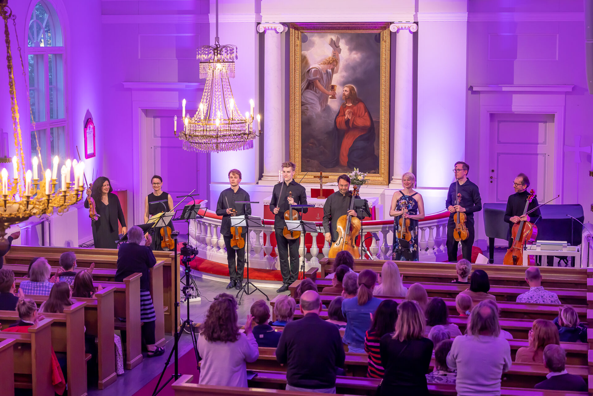 Kahdeksan jousisoittajaa ottaa vastaan aplodeja yleisön edessä Tampereen vanhassa kirkossa