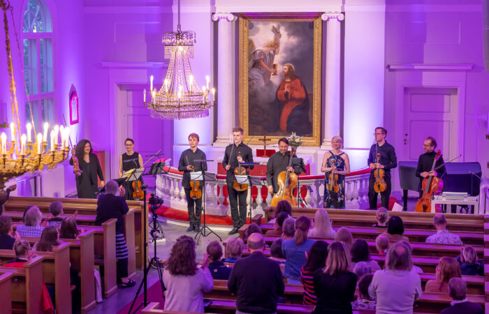 Kahdeksan jousisoittajaa ottaa vastaan aplodeja yleisön edessä Tampereen vanhassa kirkossa