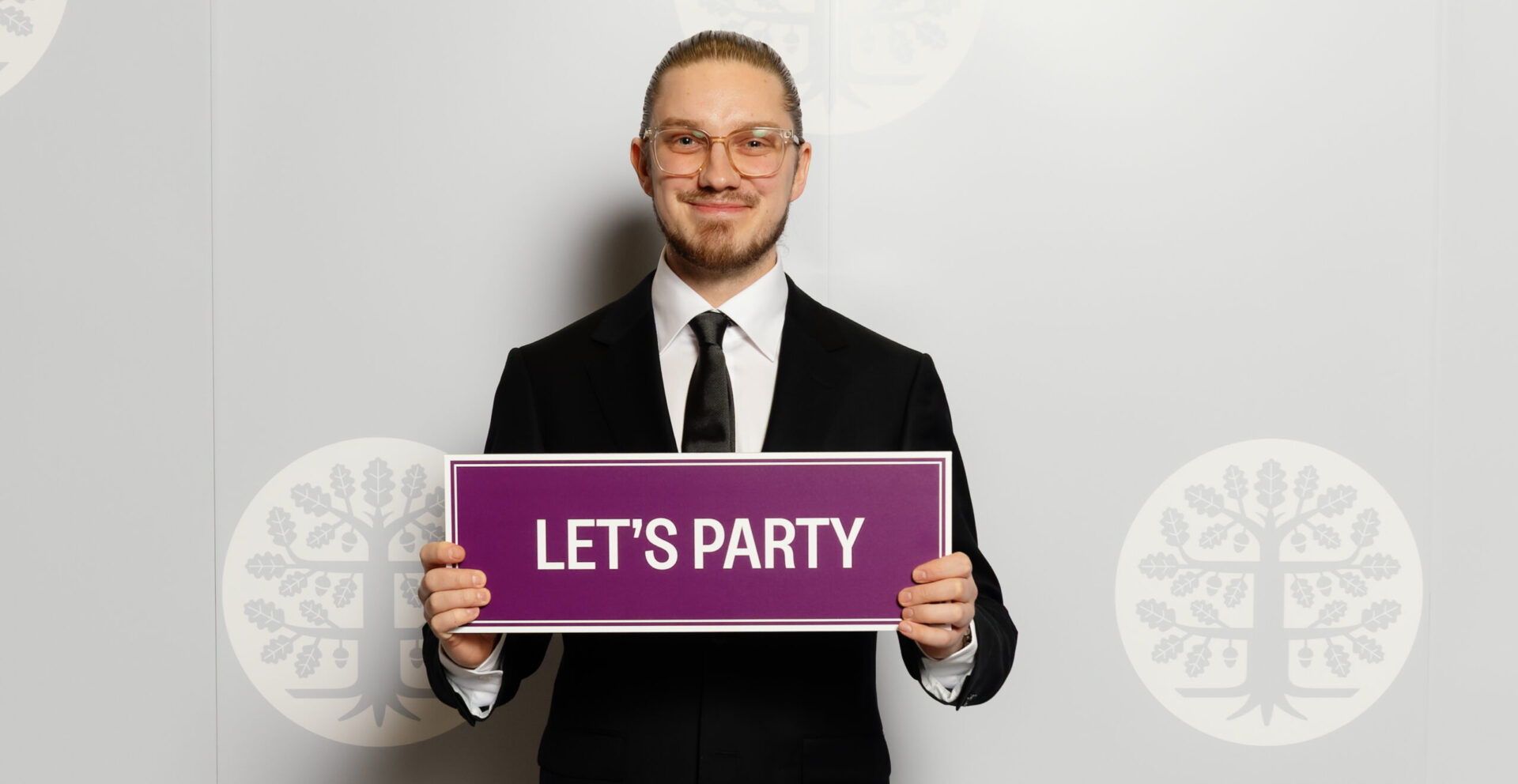 Johannes Rantanen valokuvausseinän edessä, kädessään violetti kyltti jossa lukee let's party.