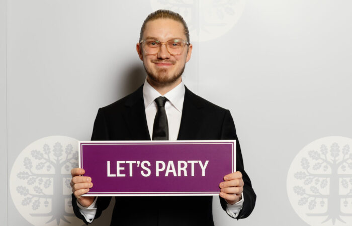 Johannes Rantanen valokuvausseinän edessä, kädessään violetti kyltti jossa lukee let's party.