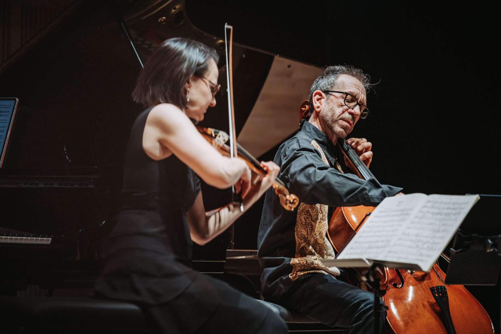 Lähikuva viulisti Réka Szilvaysta ja sellisti Robert Cohenista, jotka soittavat lavalla, nuoteista lukien.