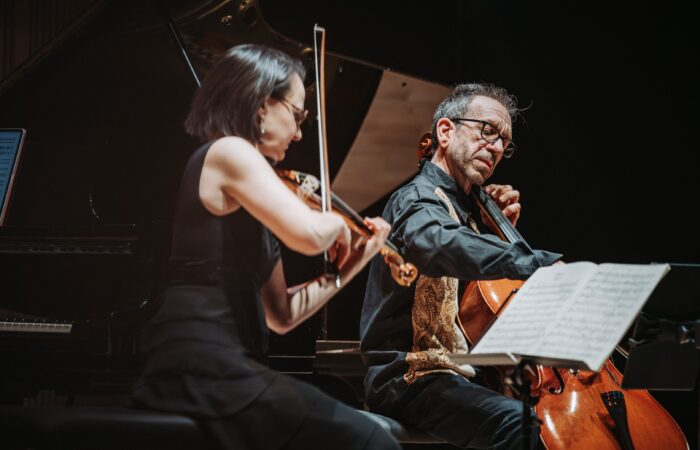 Lähikuva viulisti Réka Szilvaysta ja sellisti Robert Cohenista, jotka soittavat lavalla, nuoteista lukien.