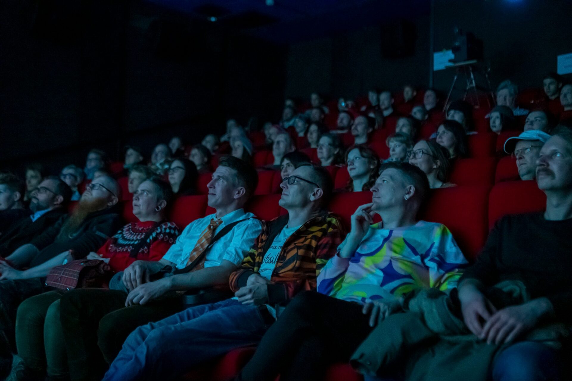 Kuva elokuvateatterisalista. Kuvassa ihmiset istuvat punaisilla penkeillä, hämärässä salissa. Kuva on otettu katsojia kohti.