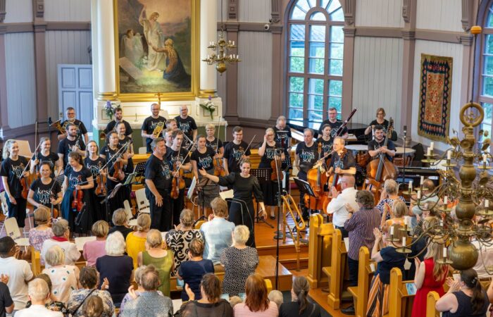 Muusikot ja kapellimestari kiittävät yleisöä konsertin jälkeen kirkon alttarin edessä.