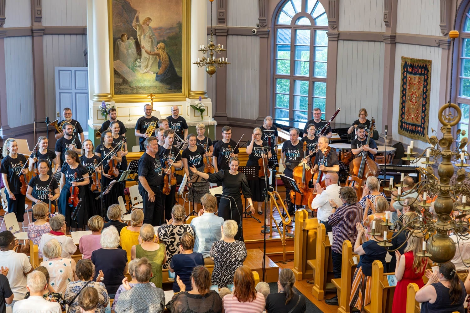 Muusikot ja kapellimestari kiittävät yleisöä konsertin jälkeen kirkon alttarin edessä.