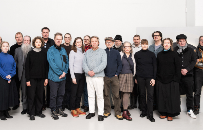 Ryhmävalokuva Mäntän kuvataideviikkojen taiteilijoista. Valokuvassa 20 henkilöä kahdessa rivissä valkoista taustaa vasten.