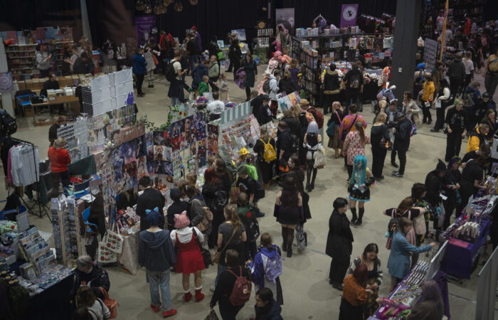 Tampere Kuplii tapahtuma Tampere-talossa. Sisätiloissa useita myyntipöytiä ja kojuja täynnä taidetta, printtejä, käsitöitä ja oheistuotteita. Paikalla on runsaasti ihmisiä kiertämässä ja selaamassa tuotteita, osa pukeutuneena värikkäisiin tai cosplay-tyylisiin asuihin.