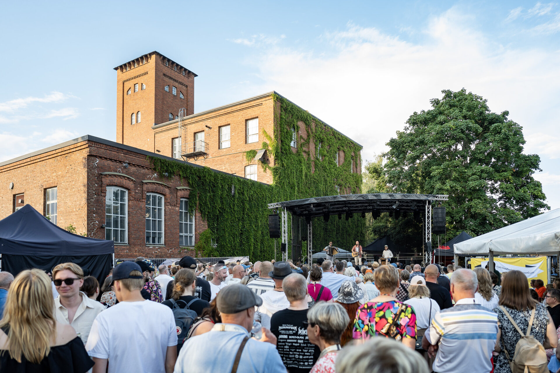 Yleisöä Työväen Musiikkitapahtumassa, taustalla tehdasrakennuksia.