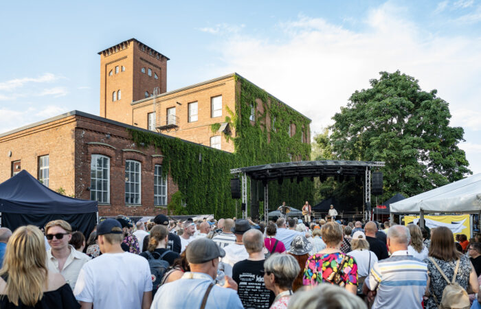 Yleisöä Työväen Musiikkitapahtumassa, taustalla tehdasrakennuksia.